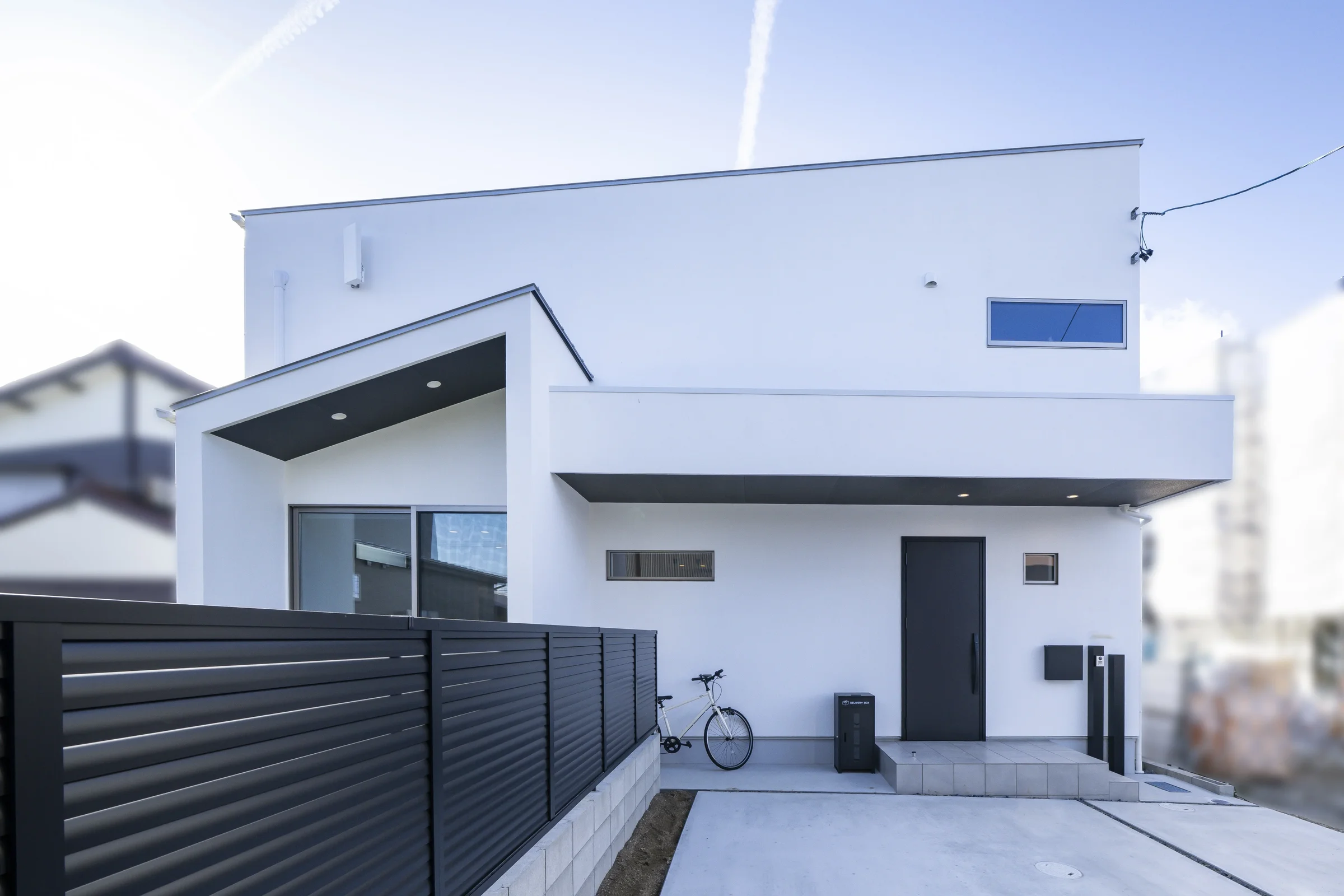 白い外壁に片流れ屋根の住宅と黒いルーバーフェンス
